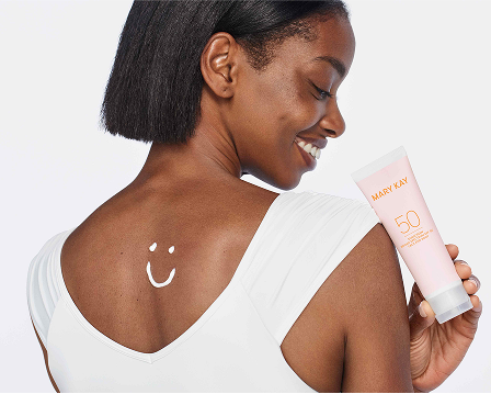Modelo sosteniendo un tubo de Mary Kay Sunscreen Broad Spectrum SPF 50, con una carita sonriente dibujada con protector solar en la parte superior de la espalda.